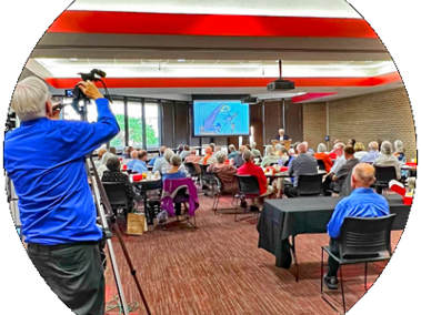 a man records a room full of people seated around tables